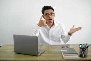 young asian businessman in a workplace making phone gesture and doubting wearing white shirt isolated on white background photo