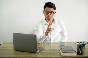 young asian businessman in a workplace frustrated and pointing to the front, wear white shirt with glasses isolated photo