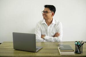 sonriente joven asiático empresario en un lugar de trabajo contento y cruzado brazos mirando el lado vestir blanco camisa con lentes aislado foto