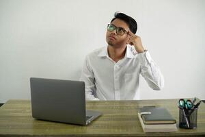 joven asiático empresario en un lugar de trabajo haciendo el gesto de Locura poniendo dedo en el cabeza vestir blanco camisa con lentes aislado foto