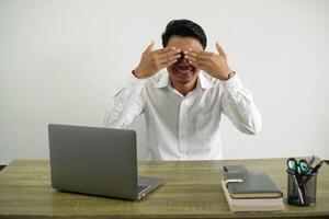 young asian businessman in a workplace covering eyes by hands wearing white shirt isolated photo