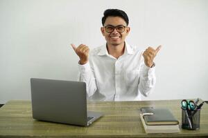 young asian businessman in a workplace with thumbs up gesture and smiling, wear white shirt with glasses isolated photo