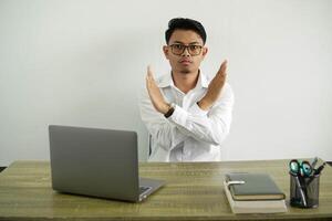 joven asiático empresario en un lugar de trabajo haciendo No gesto con ambos manos cruzado, vistiendo blanco camisa con lentes aislado foto