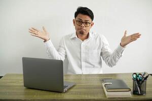 joven asiático empresario en un lugar de trabajo haciendo dudas gesto con abierto brazos, vestir blanco camisa con lentes aislado foto