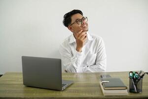 young asian businessman in a workplace thinking an idea looking up wearing white shirt with glasses isolated photo