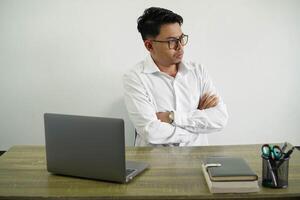 young asian businessman in a workplace making doubts gesture while lifting the shoulders wear white shirt with glasses isolated photo