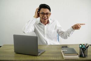 young asian businessman in a workplace surprised and pointing finger to the side wearing white shirt with glasses isolated photo