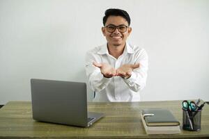 young asian businessman in a workplace holding copyspace imaginary on the palm to insert an ad, wearing white shirt with glasses isolated photo