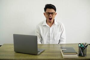 young asian businessman in a workplace shouting to the front with mouth wide open wear white shirt with glasses isolated photo