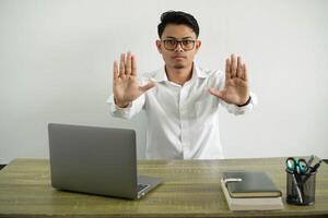 young asian businessman in a workplace making stop gesture and disappointed, wearing white shirt with glasses isolated photo