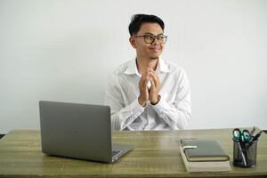 joven asiático empresario en un lugar de trabajo maquinación algo, vistiendo blanco camisa con lentes aislado foto