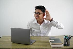 young asian businessman in a workplace listening to something by putting hand on the ear wearing white shirt isolated on white background photo