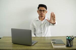 young asian businessman in a workplace making stop gesture, wearing white shirt with glasses isolated photo