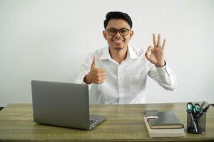 young asian businessman in a workplace showing ok sign and thumb up gesture, wear white shirt with glasses isolated photo