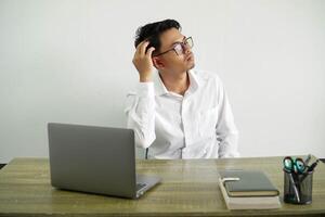 young asian businessman in a workplace having doubts while scratching head, wearing white shirt with glasses isolated photo