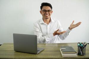 young asian businessman in a workplace extending hands to the side for inviting to come, wear white shirt with glasses isolated photo