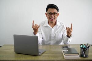 joven asiático empresario en un lugar de trabajo haciendo rock gesto vistiendo blanco camisa aislado foto