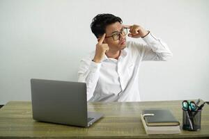 young asian businessman in a workplace having doubts and thinking, wearing white shirt with glasses isolated photo