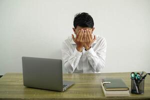 young asian businessman in a workplace cover your face with your hands, with tired and sick expression, wearing white shirt with glasses isolated photo