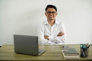 young asian businessman in a workplace keeping the arms crossed and smiling in frontal position wear white shirt with glasses isolated photo