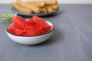 rojo en escabeche jengibre en un salsa barco en un plato en un gris antecedentes. picante alimentos salud foto