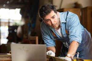 Carpenter working on laptop in his workshop at a woodworking factory photo