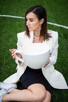 A business woman with a large cup, sitting on a green lawn in the park. photo