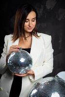 Portrait of a woman holding a silver disco ball. Taken in a photo studio.