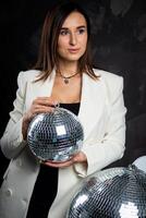 Portrait of a woman holding a silver disco ball. Taken in a photo studio.