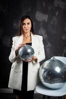 Portrait of a woman holding a silver disco ball. Taken in a photo studio.