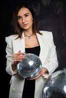 Portrait of a woman holding a silver disco ball. Taken in a photo studio.