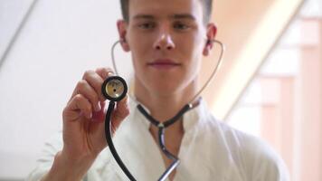 jovem estagiário posando com estetoscópio olhando às Câmera dentro médico escritório. conceito do medicamento, saúde Cuidado e pessoas video