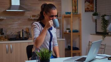 mujer sonriente y diciendo Hola durante vídeo conferencia mientras trabajando desde hogar. ocupado enfocado empleado utilizando moderno tecnología red inalámbrico haciendo tiempo extraordinario para trabajo leyendo escribiendo, buscando foto