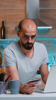 Freelancer making transaction from home using credit card sitting in the kitchen late at night. Freelancer shopping online from home with electronic paymant on digital notebook conected to internet photo