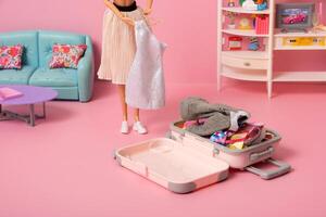 A doll puts clothes in a suitcase in a pink room. Creative travel concept photo