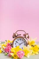 alarma reloj con amarillo y rosado flores primavera tiempo, luz ahorros concepto, primavera adelante foto