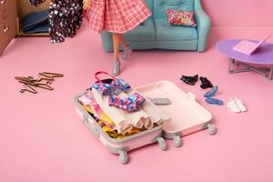 An open suitcase with clothes in the middle of the pink room where the doll puts the clothes. Travel concept photo