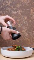 A plate of beef ribs in barbecue sauce and a woman's hands with pepper over them photo