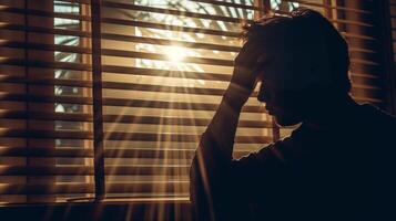 AI generated man with headache silhouetted by window, sunlight through blinds photo