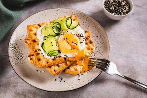 Waffles with poached egg, cucumber and sour cream on a plate on the table photo