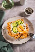 Waffles with poached egg, cucumber and sour cream on a plate on the table vertical view photo