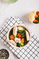 Diet soup with chicken fillet and boiled vegetables in a bowl on the table top and vertical view photo