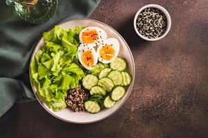 Bowl with quinoa, cucumber, boiled egg, lettuce and sesame seeds on the table top view photo