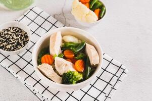 Diet soup with chicken fillet and boiled vegetables in a bowl on the table photo