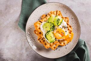 Close up of toasts with cream cheese, cucumber, poached egg and sesame seeds on a plate top view photo