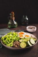 Bowl with quinoa, cucumber, boiled egg, lettuce and sesame seeds on the table vertical view photo