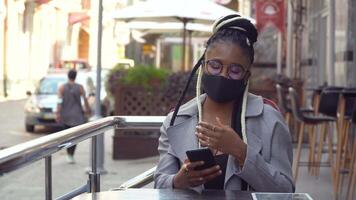 African american girl in mask chatting with friends and drinking coffee in street cafe video