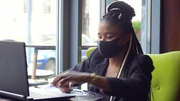 African american woman in office works on her laptop. Back at work with social distance precautions video