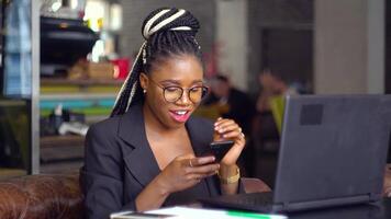 contento africano americano joven niña utilizando el teléfono mientras sentado en un café video