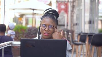 engraçado africano americano mulher dentro rua cafeteria trabalho em dela computador portátil. costas às trabalhos com social distância precauções video